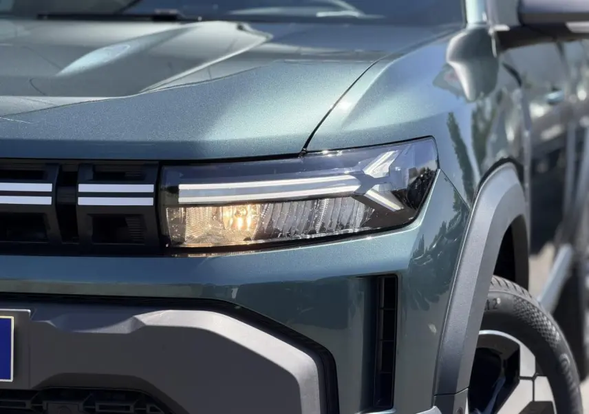 Gros plan sur l'avant droit du Dacia Duster Vert Cèdre 2026, mettant en valeur le phare LED et la calandre noire.