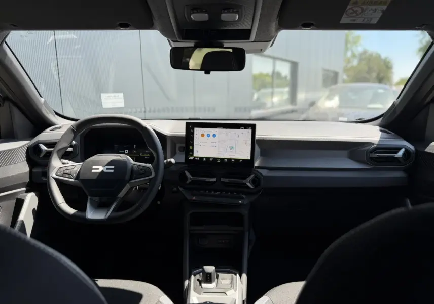 Vue intérieure frontale du tableau de bord du Dacia Duster 2026, avec écran tactile central et volant multifonction noir.