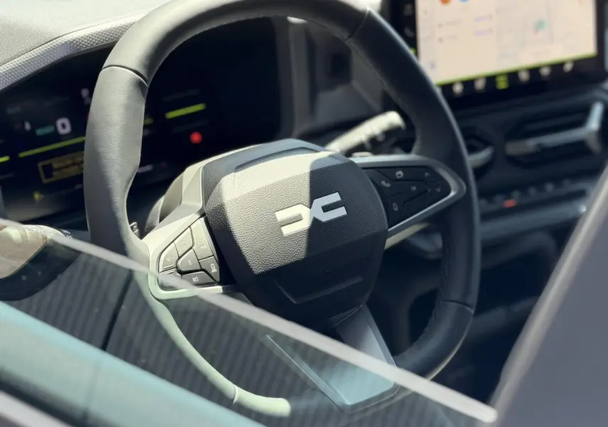 Gros plan sur le volant noir du Dacia Duster Hybrid-G 150 4x4, avec tableau de bord digital en arrière-plan.