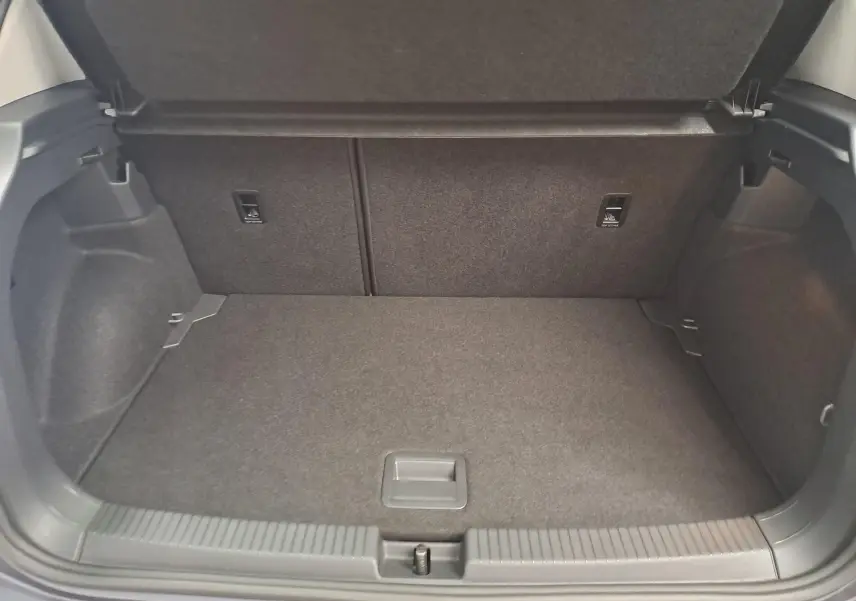 Coffre ouvert vu de l'arrière d'un Volkswagen T-Cross 2025 gris cendré, montrant l'espace de chargement vide et tapis gris.