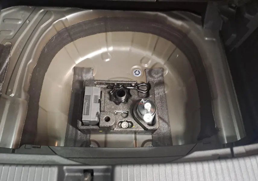 Gros plan sur le compartiment de rangement sous le coffre du Volkswagen T-Cross gris cendré, montrant les outils de bord.