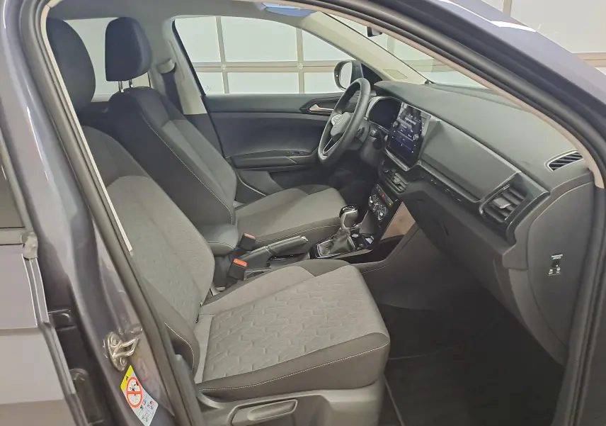 Vue intérieure côté gauche du Volkswagen T-Cross gris cendré 2025, montrant les sièges avant et le tableau de bord moderne.