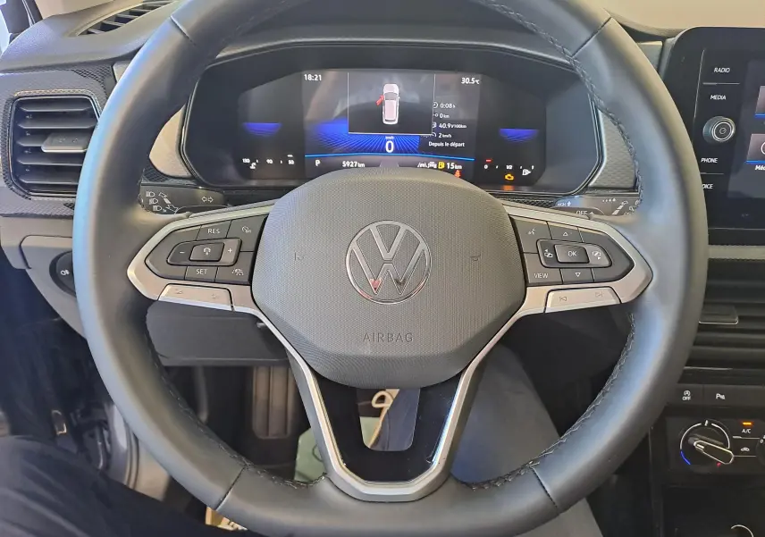 Vue rapprochée du volant multifonction noir d’un Volkswagen T-Cross 2025 avec tableau de bord digital allumé.