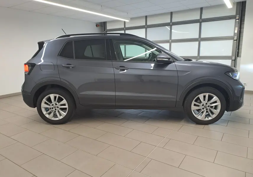 Vue de profil côté gauche d'un Volkswagen T-Cross 2025 gris cendré métallisé, avec jantes alliage et toit noir.