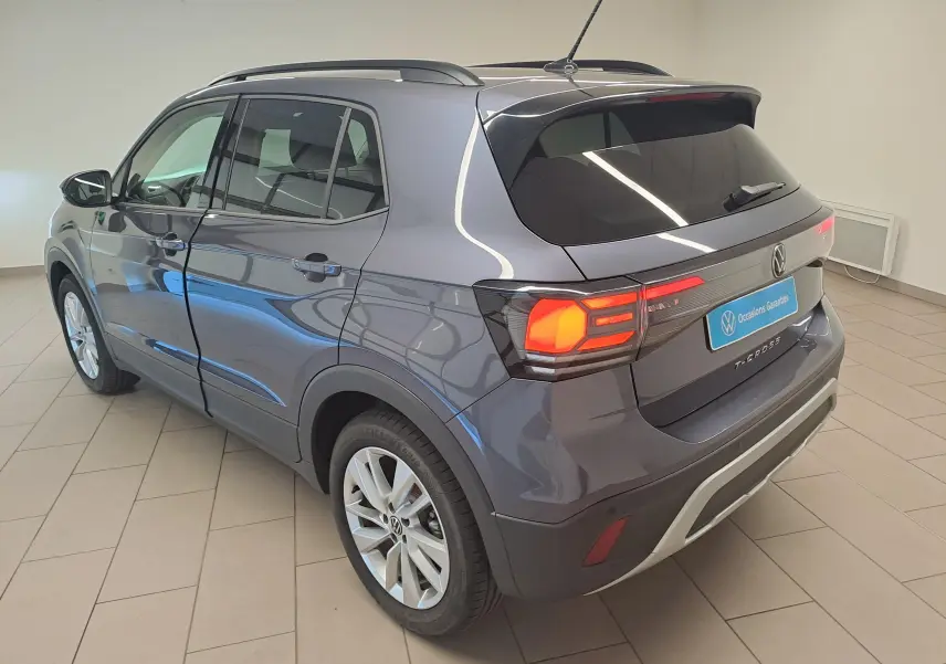 Vue 3/4 arrière droite du Volkswagen T-Cross gris cendré métallisé avec feux arrière allumés en intérieur showroom.