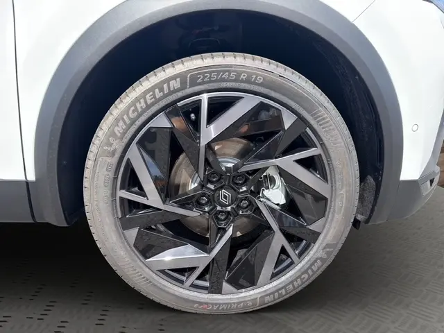 Gros plan sur la roue avant droite du Renault Captur blanc, jante noire brillante au design géométrique distinctif.