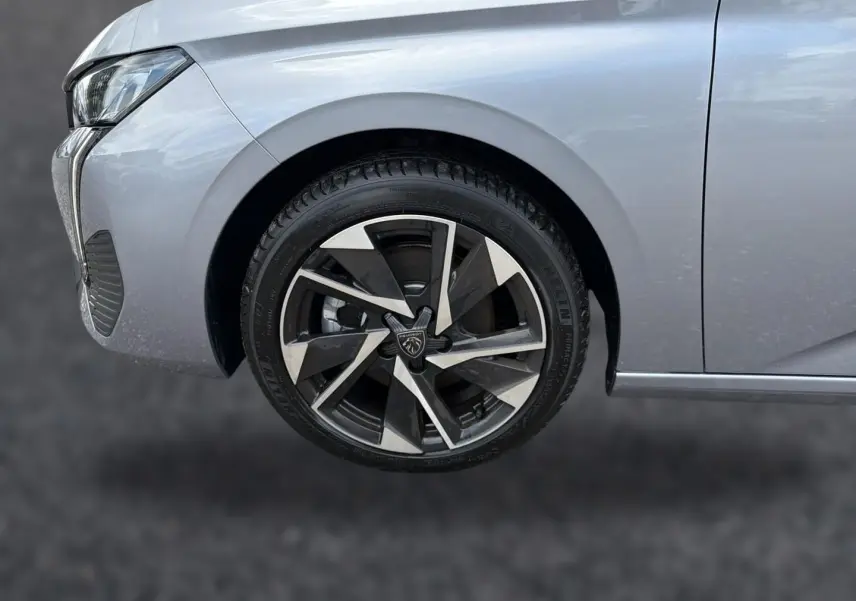 Gros plan sur la roue avant gauche et partie du pare-chocs gris d'une Peugeot 308 SW 2025 avec jante alu au design moderne.