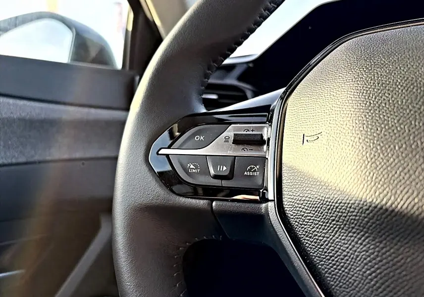 Gros plan sur le volant cuir côté gauche du Peugeot 408 Hybrid 145 allure e-dcs6 noir, avec commandes intégrées.