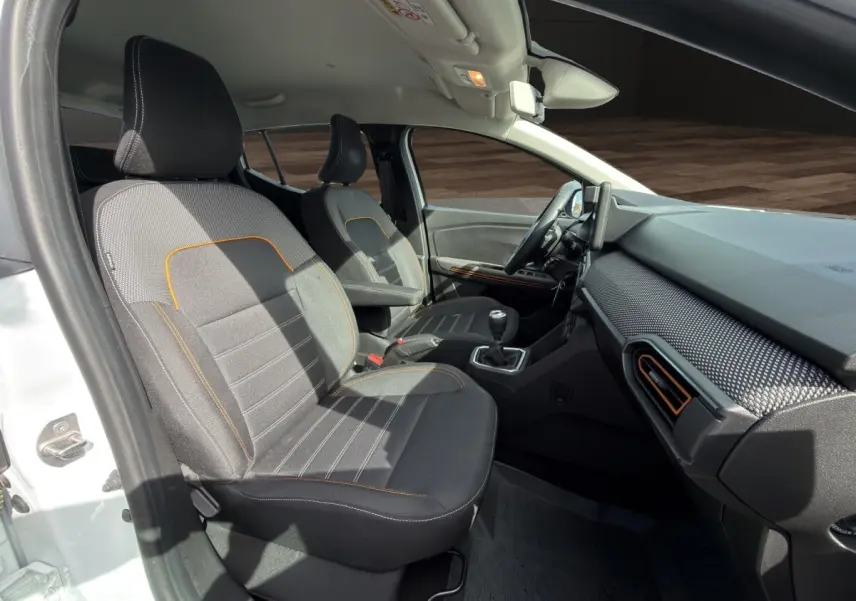Vue intérieure côté conducteur de la Dacia Sandero Stepway blanche, sièges gris avec surpiqûres orange et tableau de bord moderne.