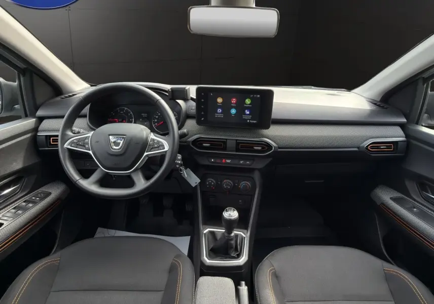 Vue intérieure frontale du tableau de bord de la Dacia Sandero Stepway blanche avec écran tactile central et volant multifonctions.