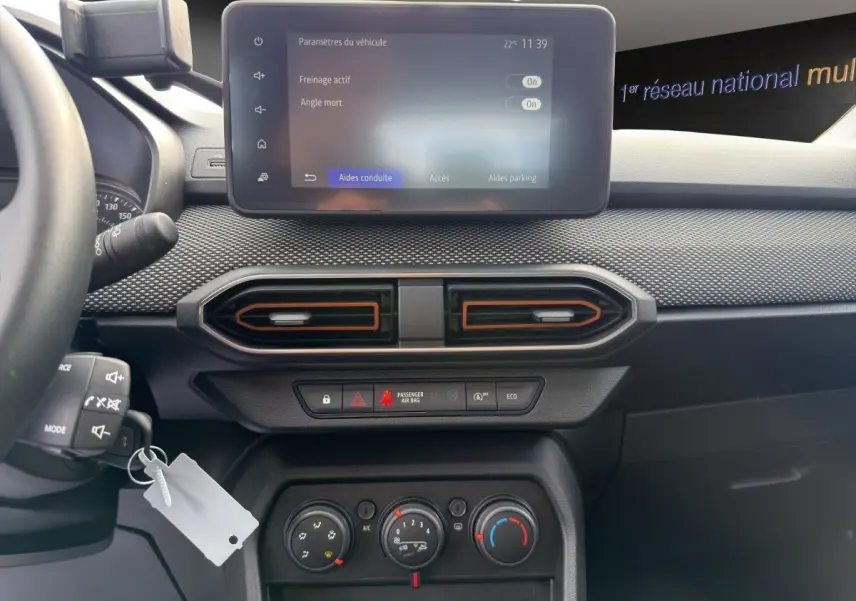 Vue intérieure du tableau de bord de la Dacia Sandero Stepway blanc, avec écran tactile central et aérateurs hexagonaux.