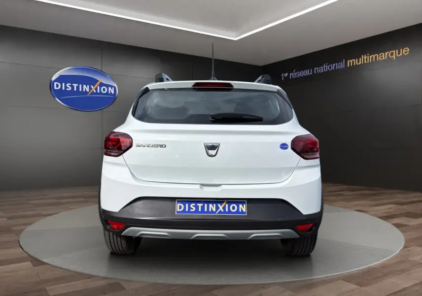 Vue arrière d'une Dacia Sandero Stepway blanche 2022, avec logo et feux arrière rouges visibles en intérieur showroom.