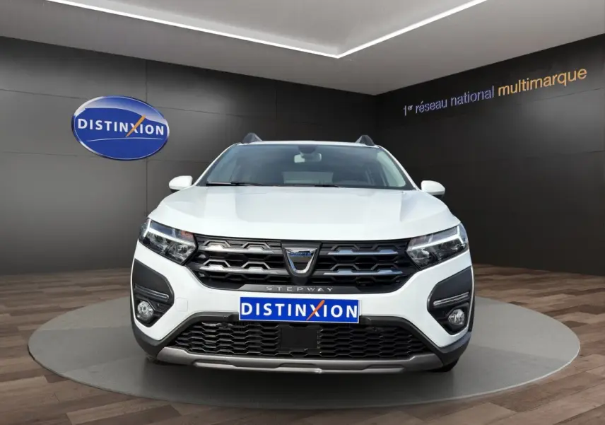 Vue frontale d'une Dacia Sandero Stepway blanche avec calandre noire et feux LED dans un showroom.