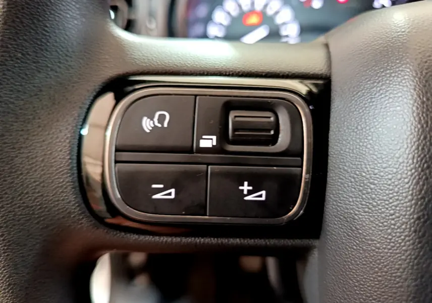 Gros plan sur les commandes de volume et téléphone au volant noir d'une Citroën C3 blanche de 2019.