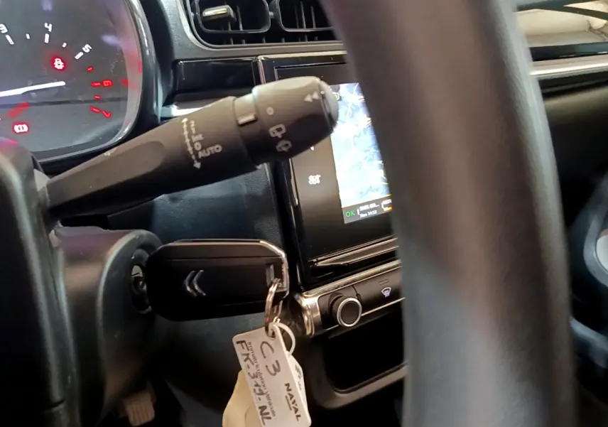 Gros plan intérieur sur le volant et la clé de contact d'une Citroën C3 blanche, avec écran tactile de navigation visible.