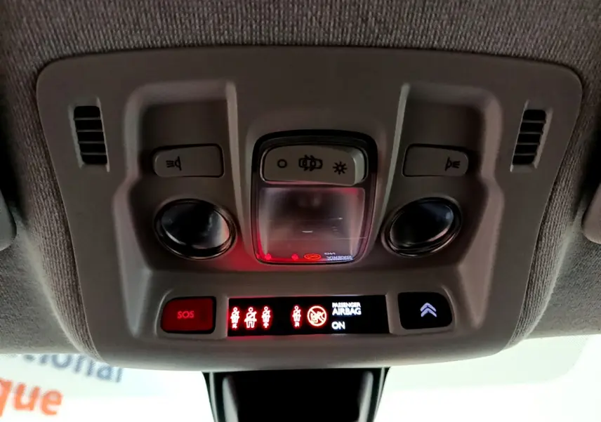 Vue en contre-plongée du plafonnier gris avec commandes d’éclairage et indicateurs lumineux allumés dans une Citroën C3 blanche.