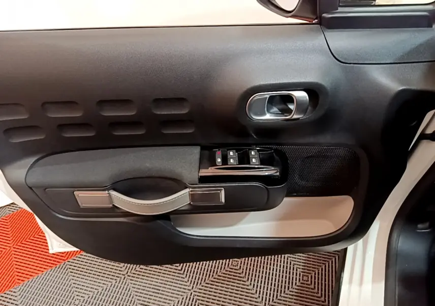 Intérieur côté gauche de la porte d'une Citroën C3 blanche 2019, avec commandes de vitres et poignée noire.