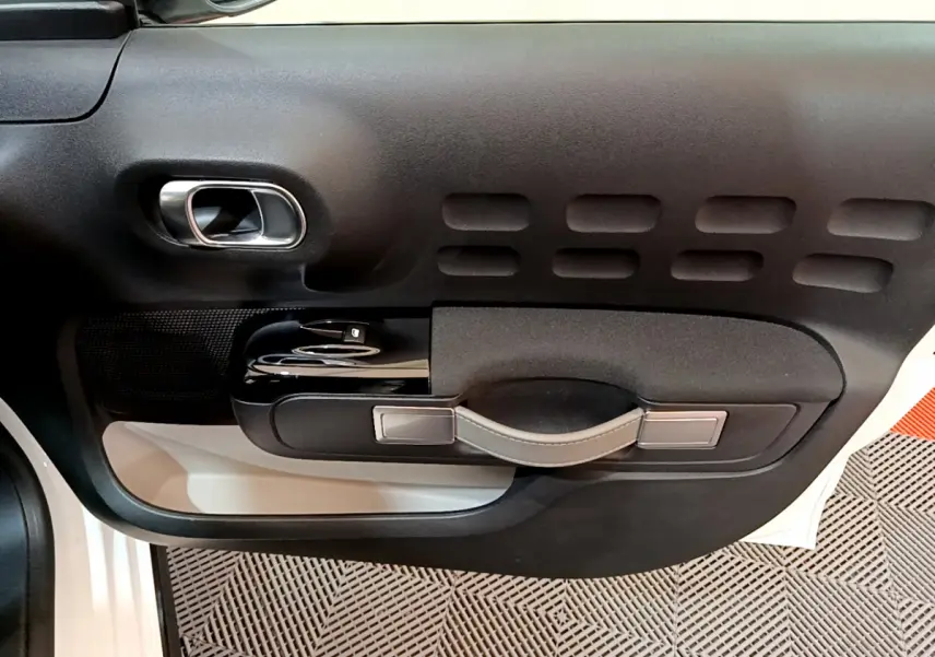 Détail de la porte côté gauche noire avec poignée en cuir et commandes de vitre d'une Citroën C3 blanche 2019.