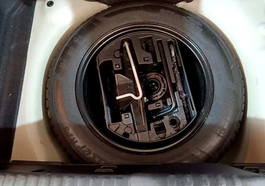 Vue plongeante sur la roue de secours noire et ses outils dans le coffre blanc d'une Citroën C3 2019 PureTech.