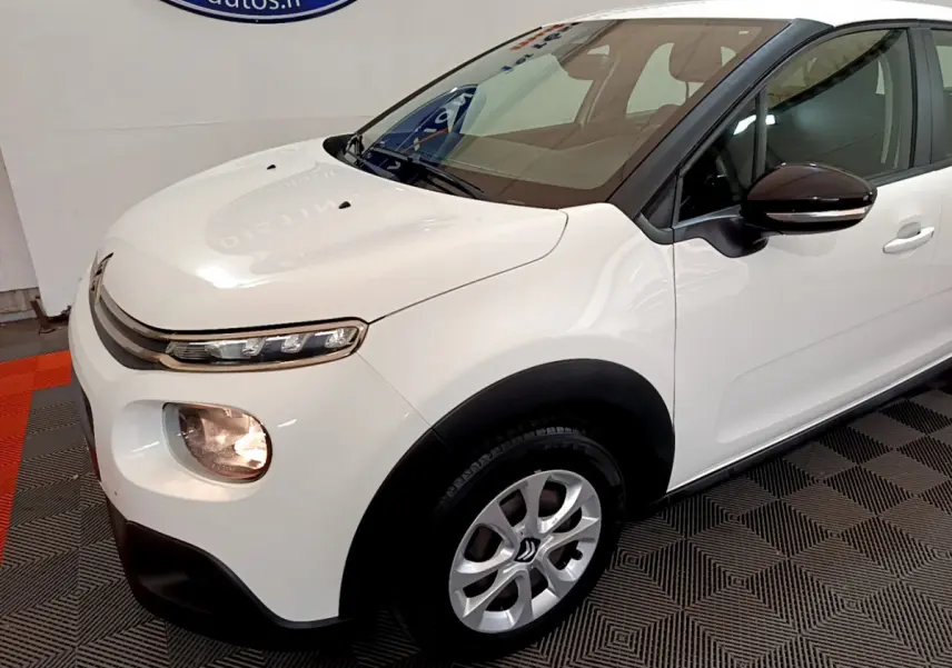 Vue 3/4 avant droit d'une Citroën C3 blanche avec rétroviseurs noirs et jantes alliage en intérieur showroom.