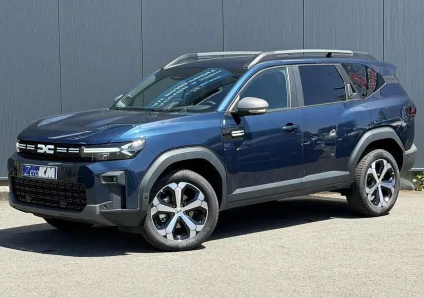 SUV Dacia Bigster bleu indigo en 3/4 avant droit avec barres de toit et jantes alliage diamantées.
