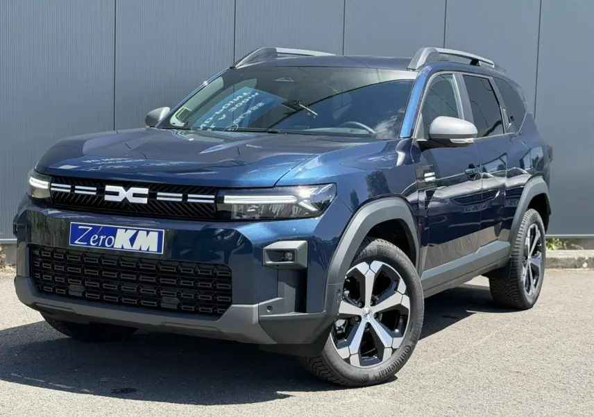 SUV Dacia Bigster bleu indigo en 3/4 avant droit avec jantes alliage et barres de toit gris mégalithe.