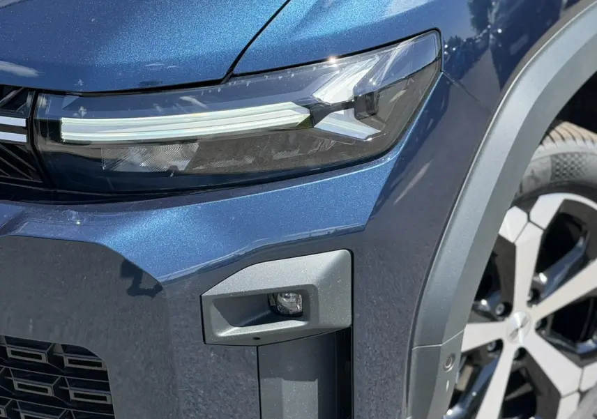 Gros plan sur l'avant droit bleu indigo du Dacia Bigster Hybrid-G 150, mettant en valeur le phare LED et la jante alliage 18 pouces.