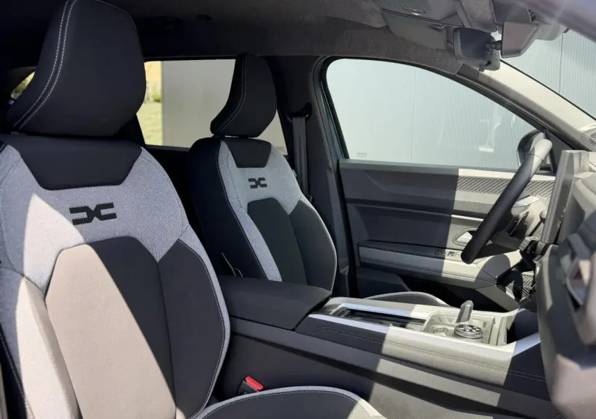Vue intérieure côté droit du DACIA BIGSTER 2026, sièges avant bicolores avec logo DC, volant et console centrale visibles.
