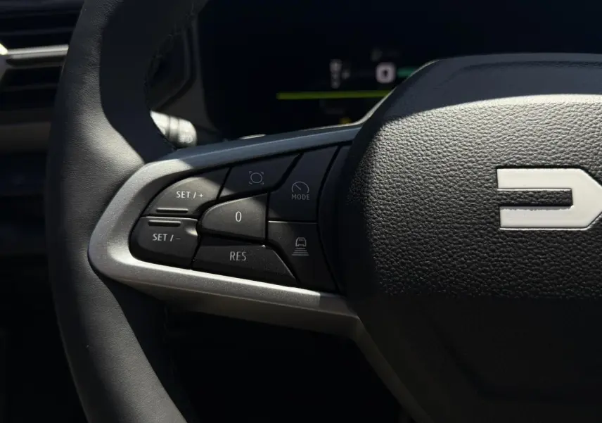 Gros plan sur les commandes à gauche du volant noir du Dacia Bigster Hybrid-G 150 4x4, avec logo Dacia visible.