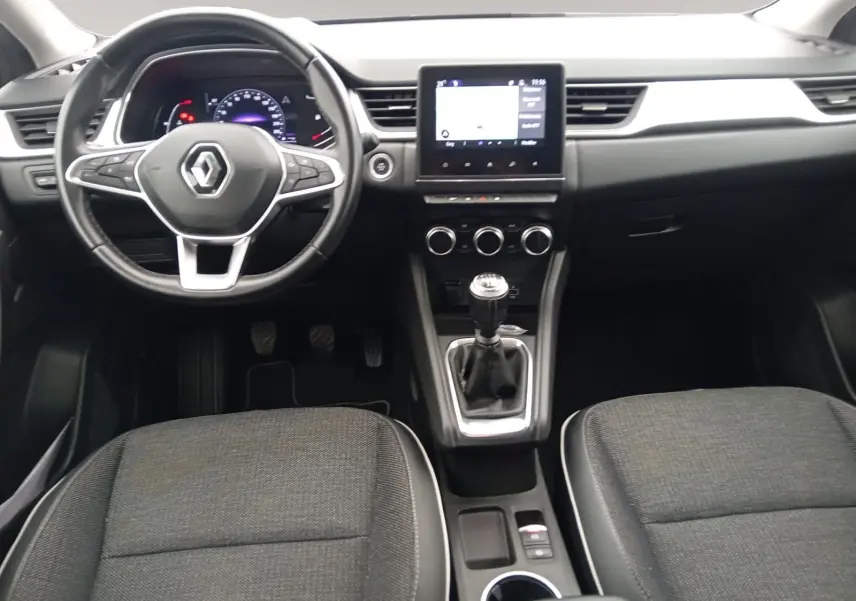 Vue intérieure frontale du tableau de bord du Renault Captur 2023 avec volant multifonction, écran tactile et levier de vitesse manuel.