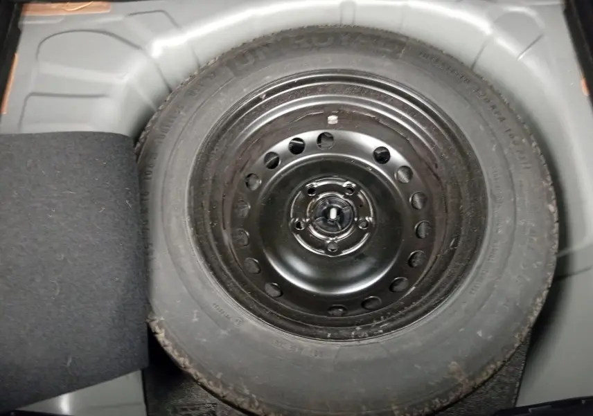 Pneu de secours noir monté dans le coffre d'un Renault Captur 1.3 Mild Hybrid 140 Techno gris cassiopée.