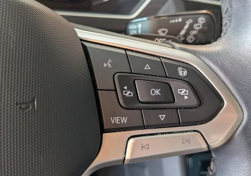 Gros plan sur les commandes du volant côté gauche du Volkswagen Tiguan noir, boutons multifonctions avec finition argentée.