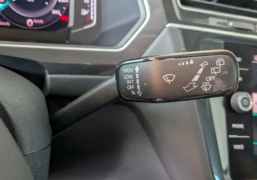 Gros plan sur la manette d’essuie-glace côté droit du volant d’un Volkswagen Tiguan noir, tableau de bord partiellement visible.