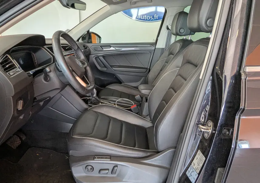Vue intérieure côté conducteur du Volkswagen Tiguan noir 2021, sièges cuir noirs avec réglages électriques et volant multifonction.