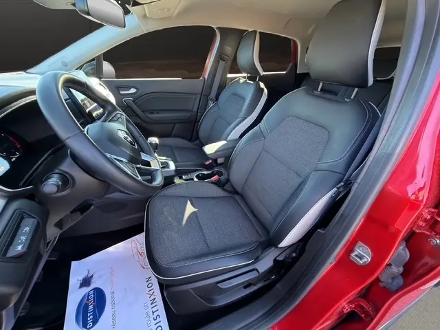 Vue intérieure côté conducteur du Renault Captur rouge 2024, mettant en valeur les sièges tissu et le volant multifonctions.