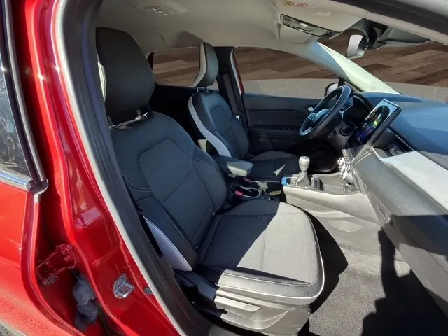 Vue intérieure côté conducteur du Renault Captur rouge 2024, montrant les sièges tissu gris et la console avec écran tactile.