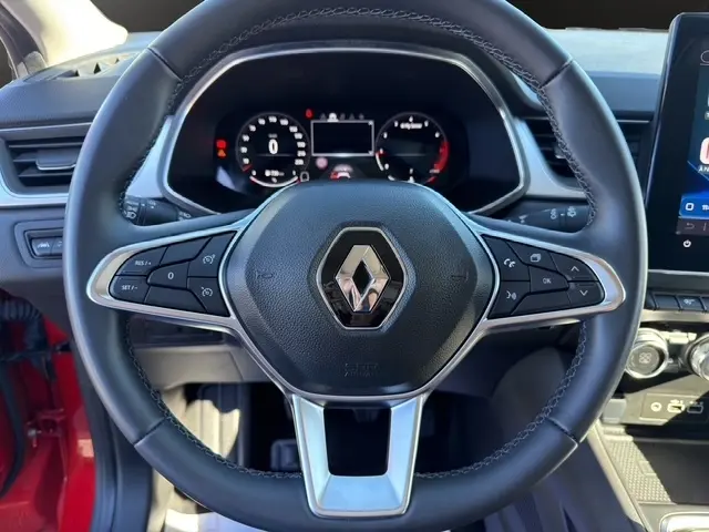 Gros plan sur le volant multifonctions noir du Renault Captur rouge 2024 avec tableau de bord numérique et écran tactile visible.