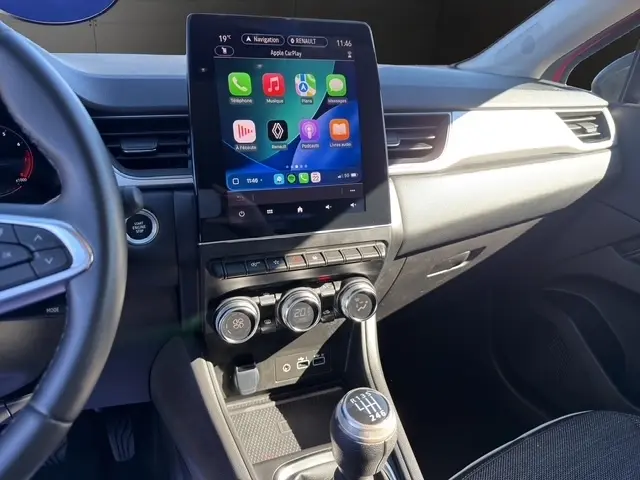 Vue intérieure côté conducteur du tableau de bord du Renault Captur rouge 2024, avec écran tactile central et boîte manuelle.