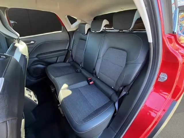 Vue intérieure côté arrière droit du Renault Captur rouge 2024, montrant la banquette arrière en tissu et cuir noir.