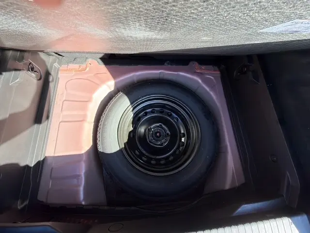 Vue plongeante sur la roue de secours noire dans le coffre rouge du Renault Captur 2024 version techno TCe 90.