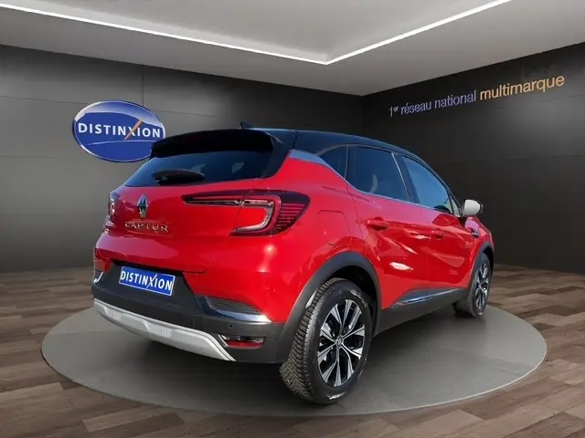Vue 3/4 arrière droite d'un Renault Captur rouge 2024 avec toit noir et jantes alliage bicolores.