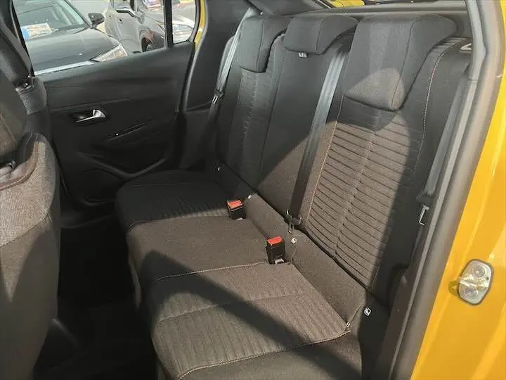 Intérieur arrière de la Peugeot 208 jaune Faro Métal, montrant les sièges noirs et la portière côté droit ouverte.