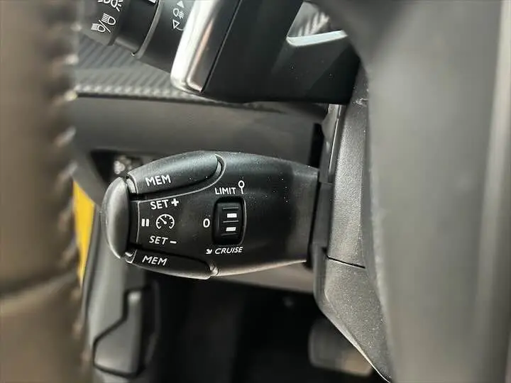 Gros plan sur la commande de régulateur de vitesse à gauche du volant d'une Peugeot 208 jaune Faro Metal.