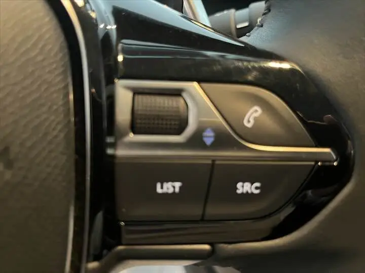 Gros plan sur les commandes au volant de la Peugeot 208 1.2 essence, boutons LIST, SRC et téléphone visibles.