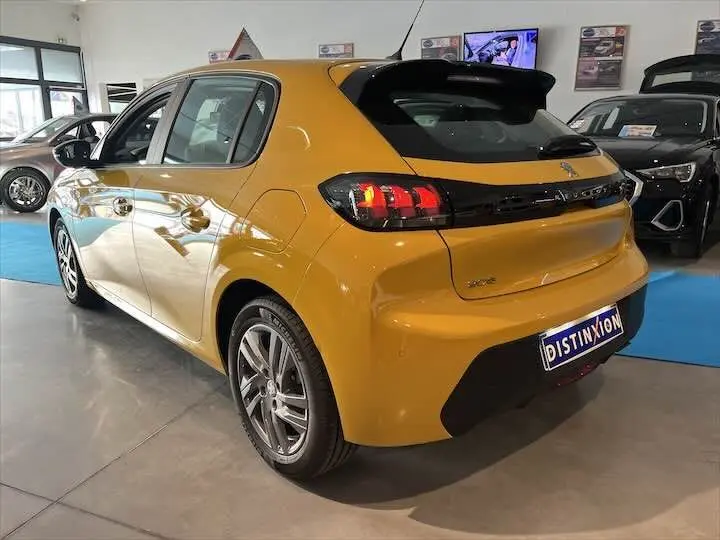 Vue 3/4 arrière d'une Peugeot 208 jaune Faro Metal en showroom, mettant en valeur ses feux arrière LED et sa silhouette compacte.