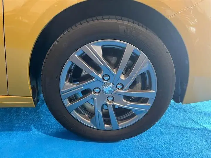 Gros plan sur la roue avant droite d'une Peugeot 208 jaune Faro Métal avec jante alliage au design moderne.