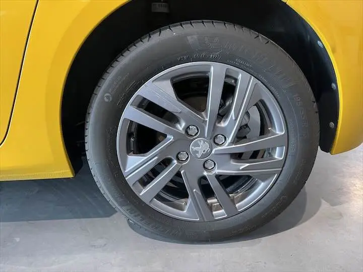 Gros plan sur la roue avant gauche d'une Peugeot 208 jaune Faro Metal avec jante alliage gris et logo lion central.