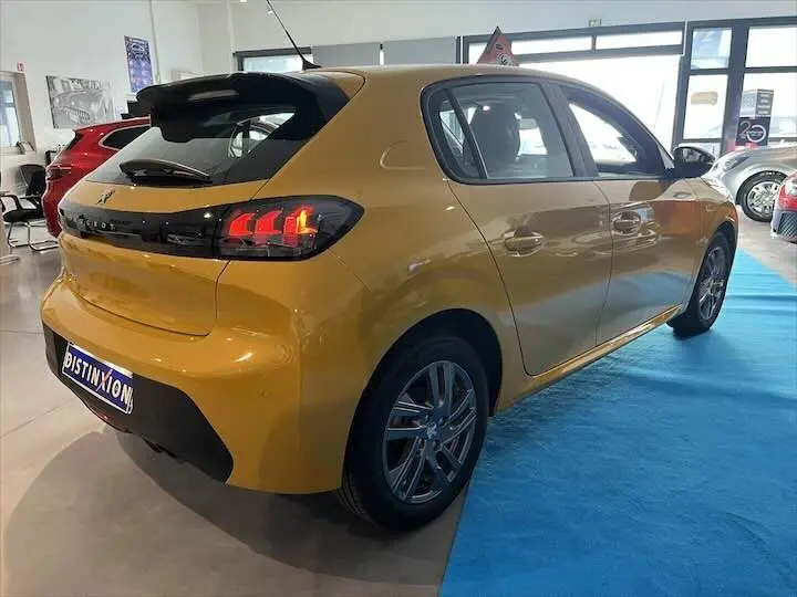 Vue 3/4 arrière droite d'une Peugeot 208 jaune Faro Metal en showroom avec feux arrière allumés.