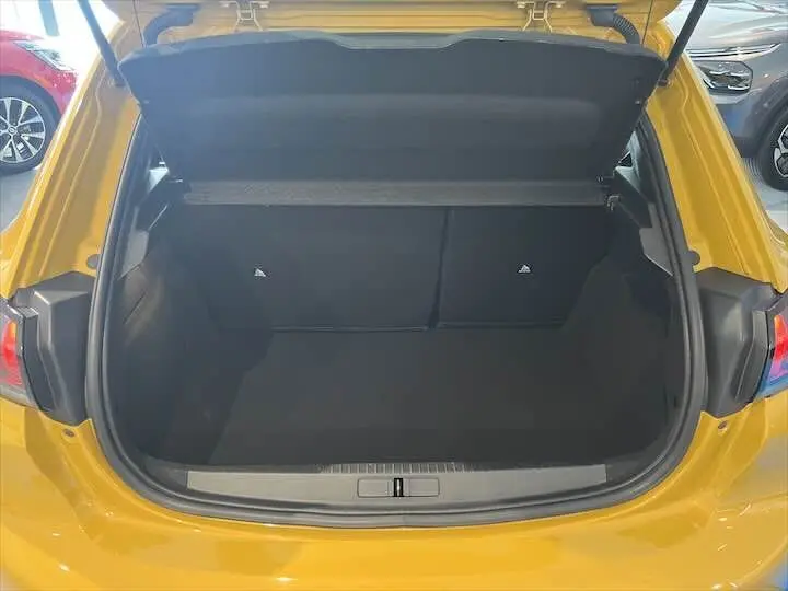 Coffre ouvert vu de l'arrière d'une Peugeot 208 jaune Faro Metal, montrant l'espace de chargement vide.