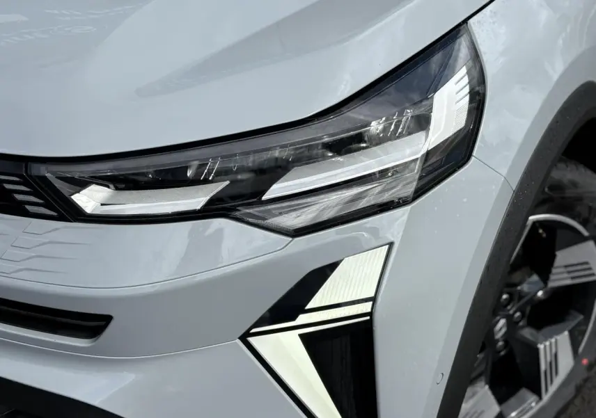 Gros plan sur le phare avant droit et la calandre d'une Renault SYMBIOZ gris clair avec jante noire.